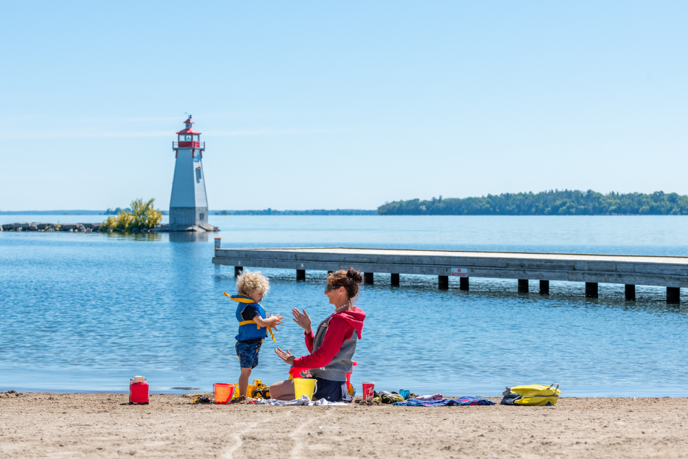 mother and child playing in the sand with a light house and a small pier in the background